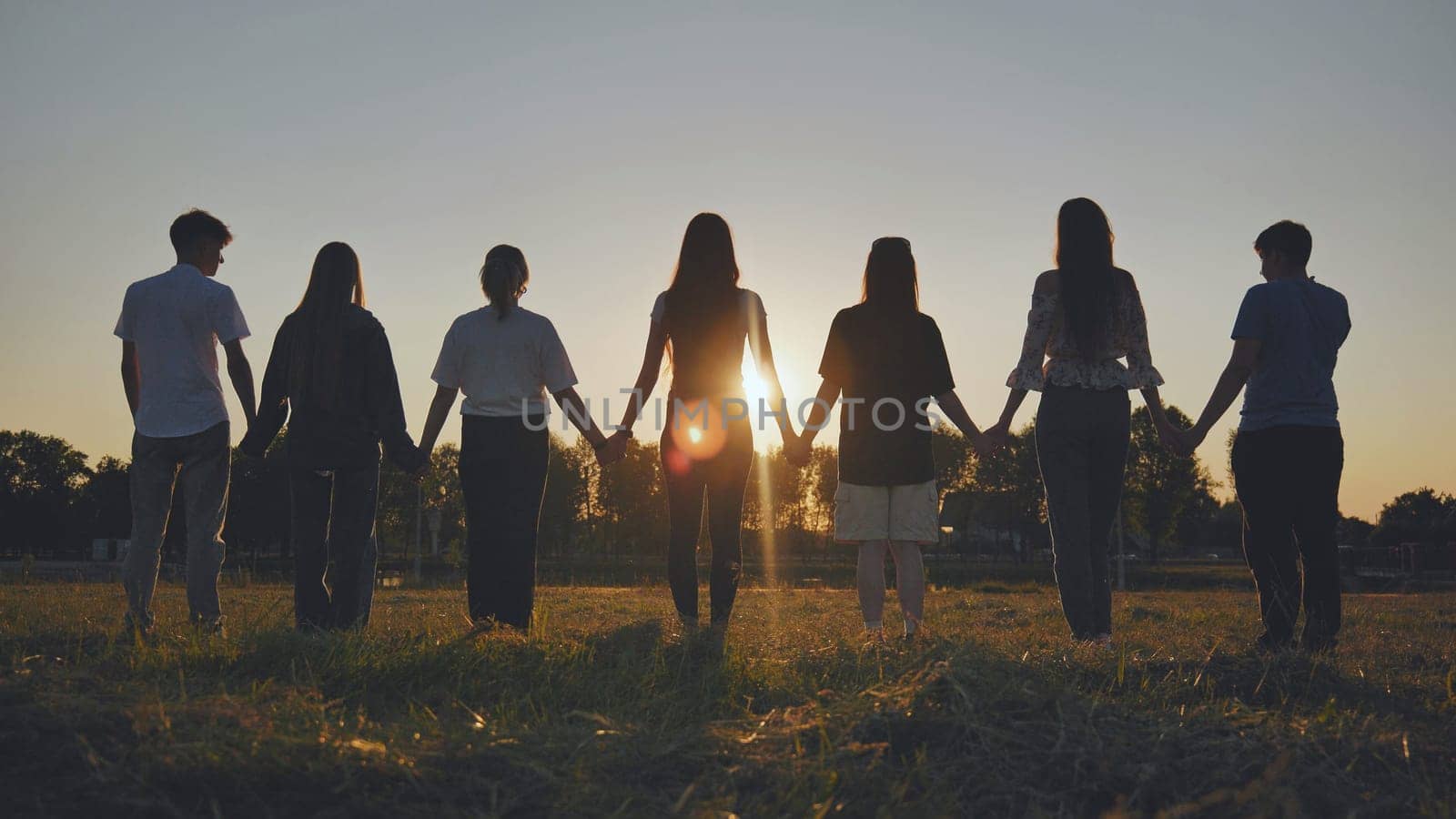 Friends standing holding hands at sunset. by DovidPro