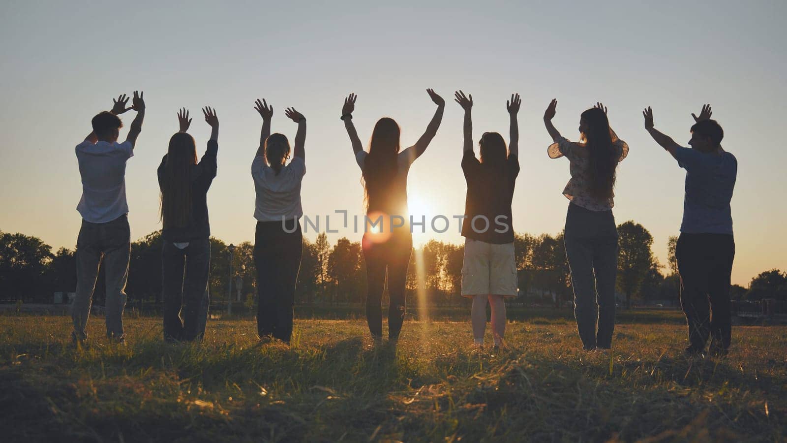 Young friends stand at sunset and wave their hands at the sun