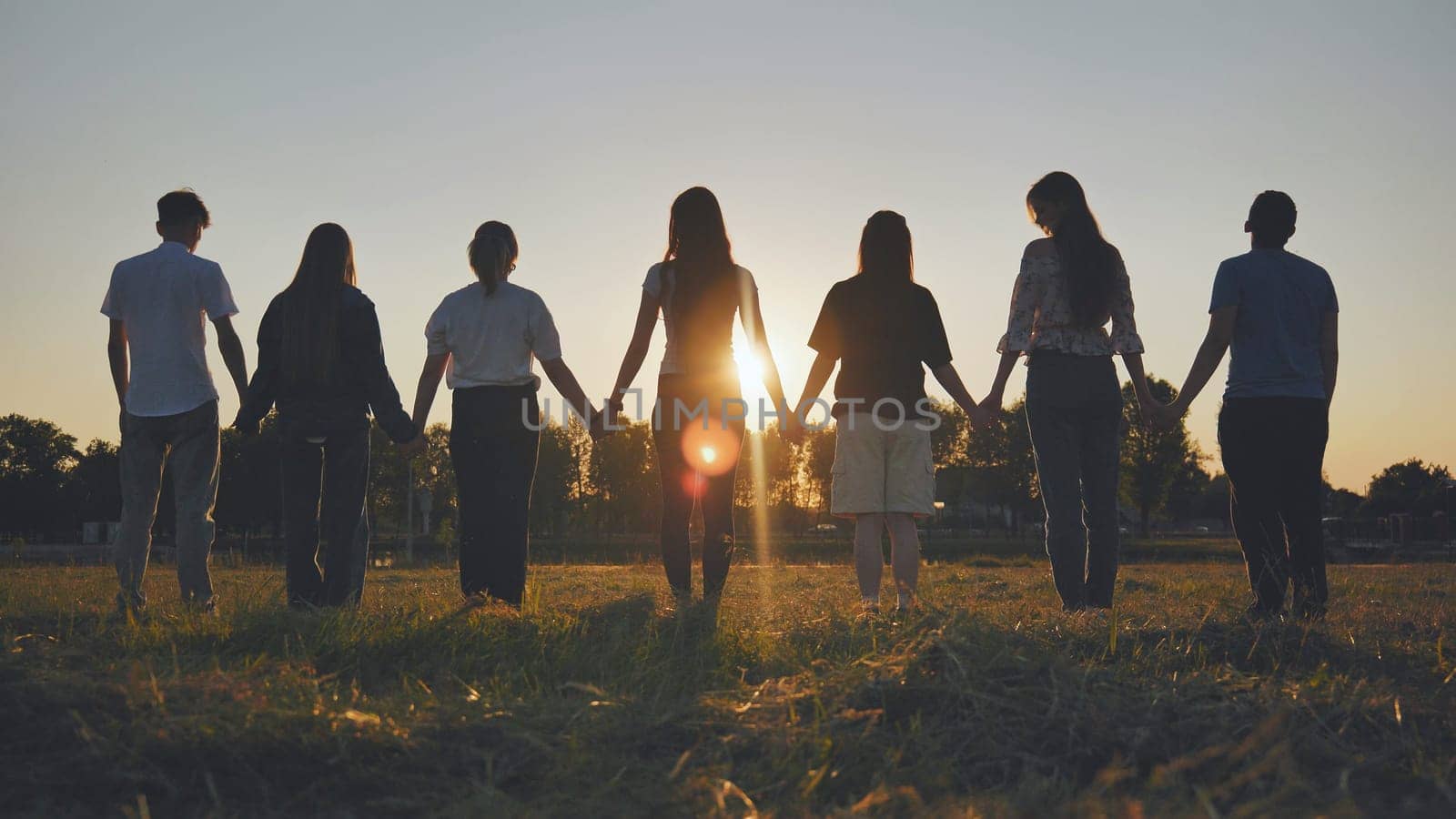 Friends standing holding hands at sunset. by DovidPro