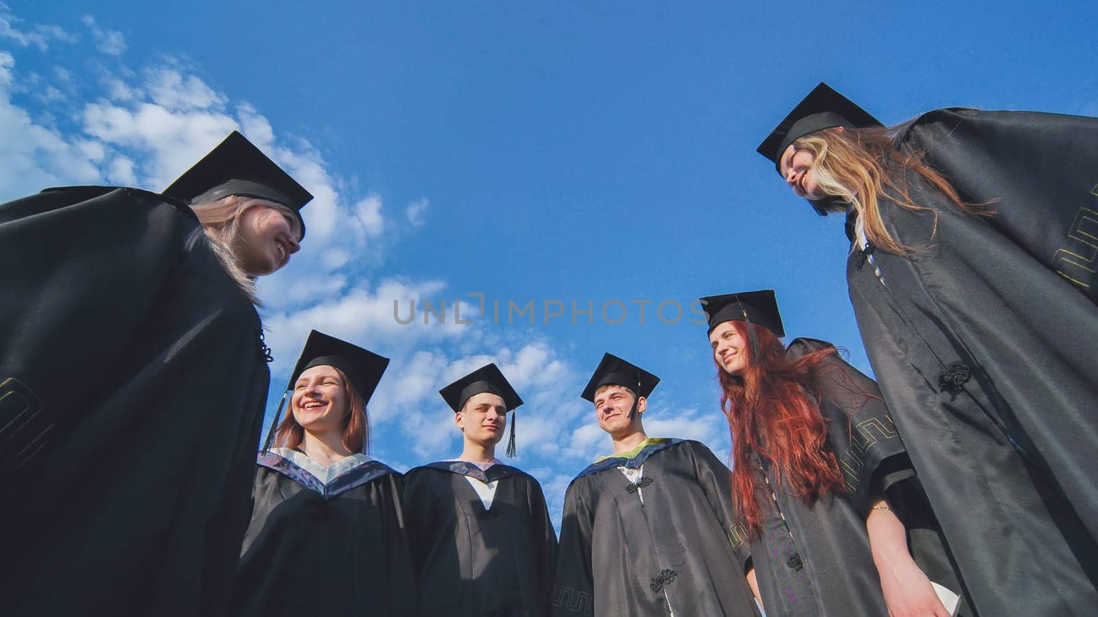 Graduating students stand in a semicircle on a sunny summer afternoon