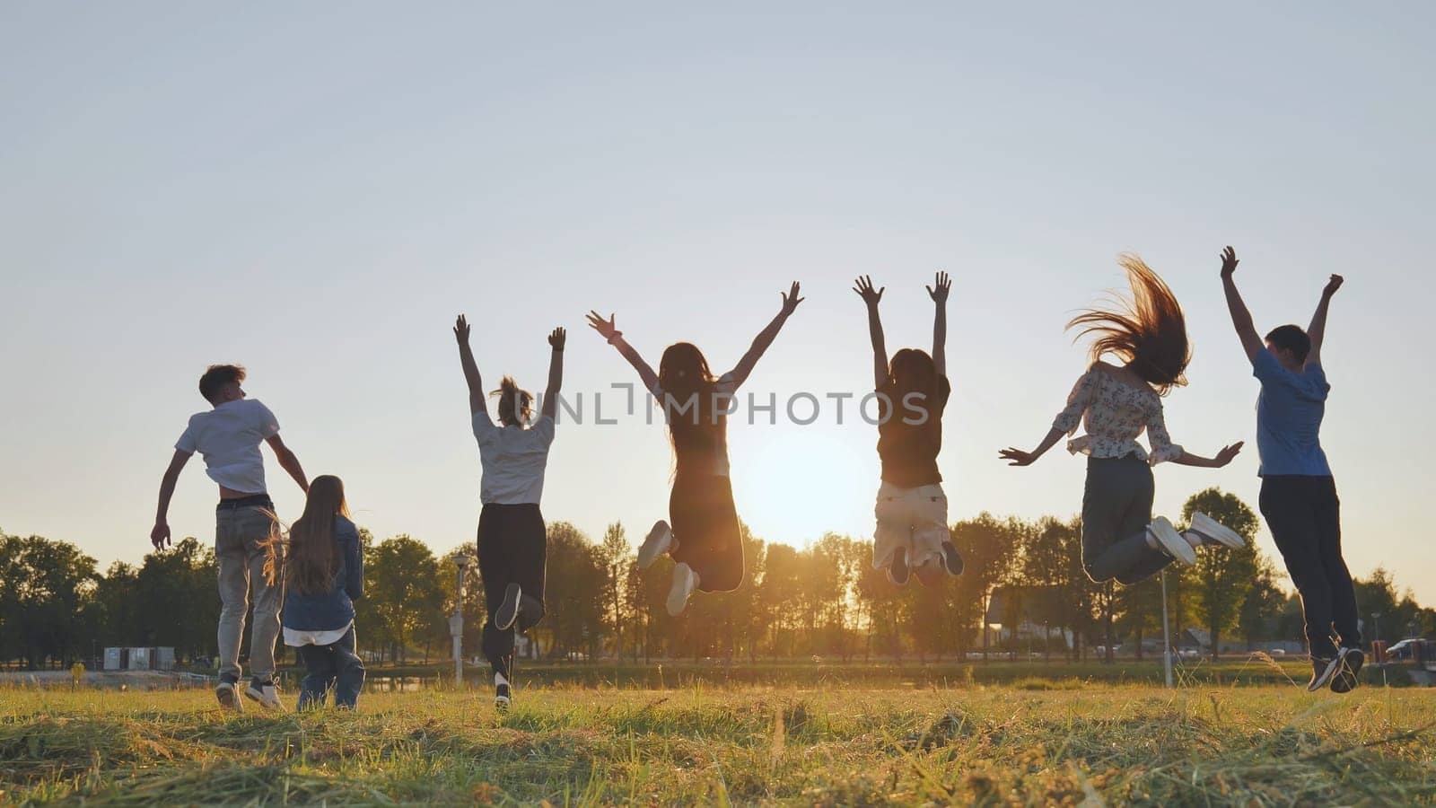 Group of five happy friends jumps at sunset time on background mountains