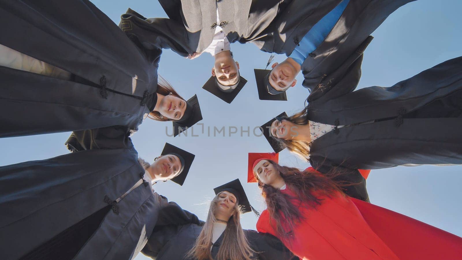 College graduates in a circle stand hugging each other