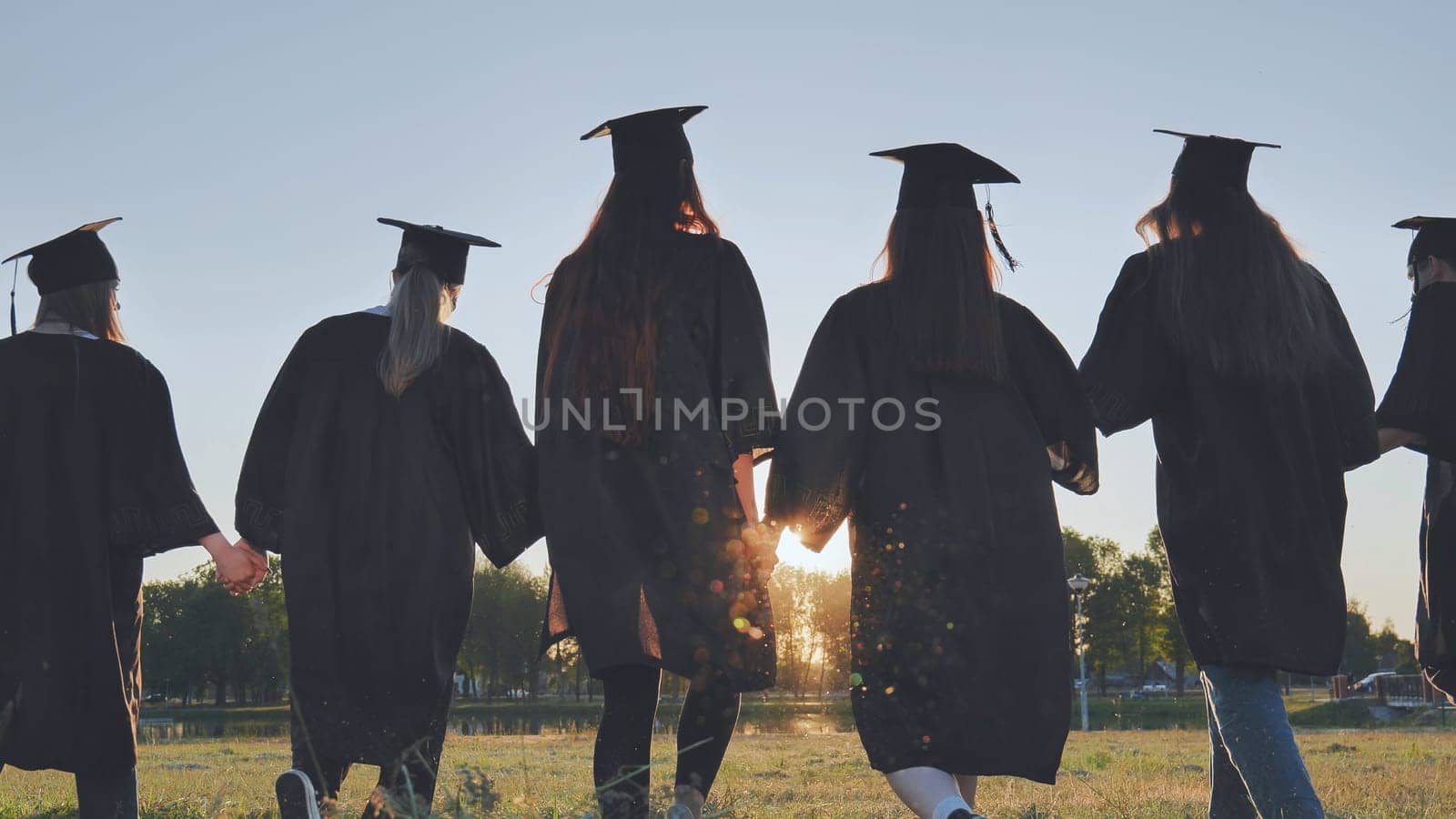 Graduate students walking through an evening meadow at sunset. by DovidPro