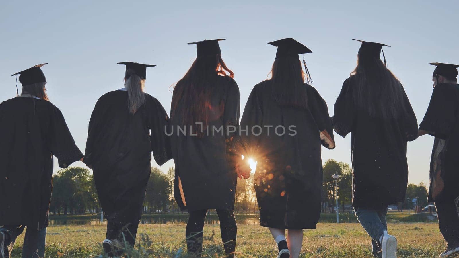 College graduates walk at sunset holding hands