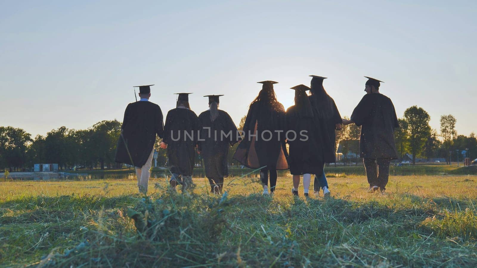 College graduates walk at sunset holding hands