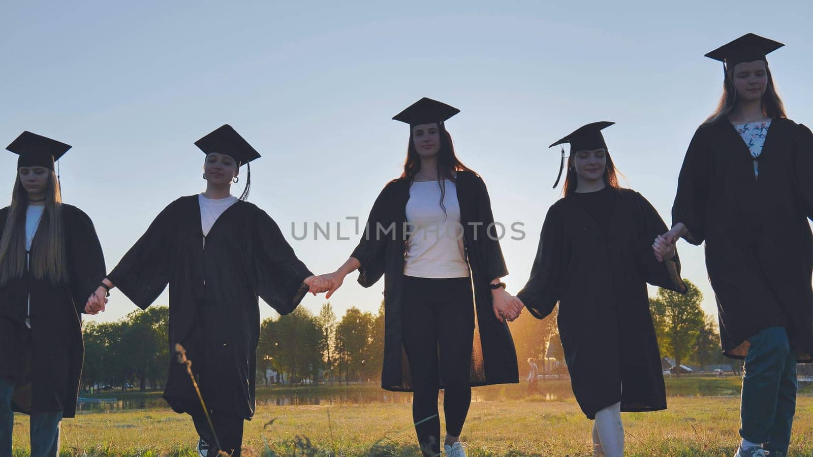 College graduates hold hands at sunset to meet the future and the sun
