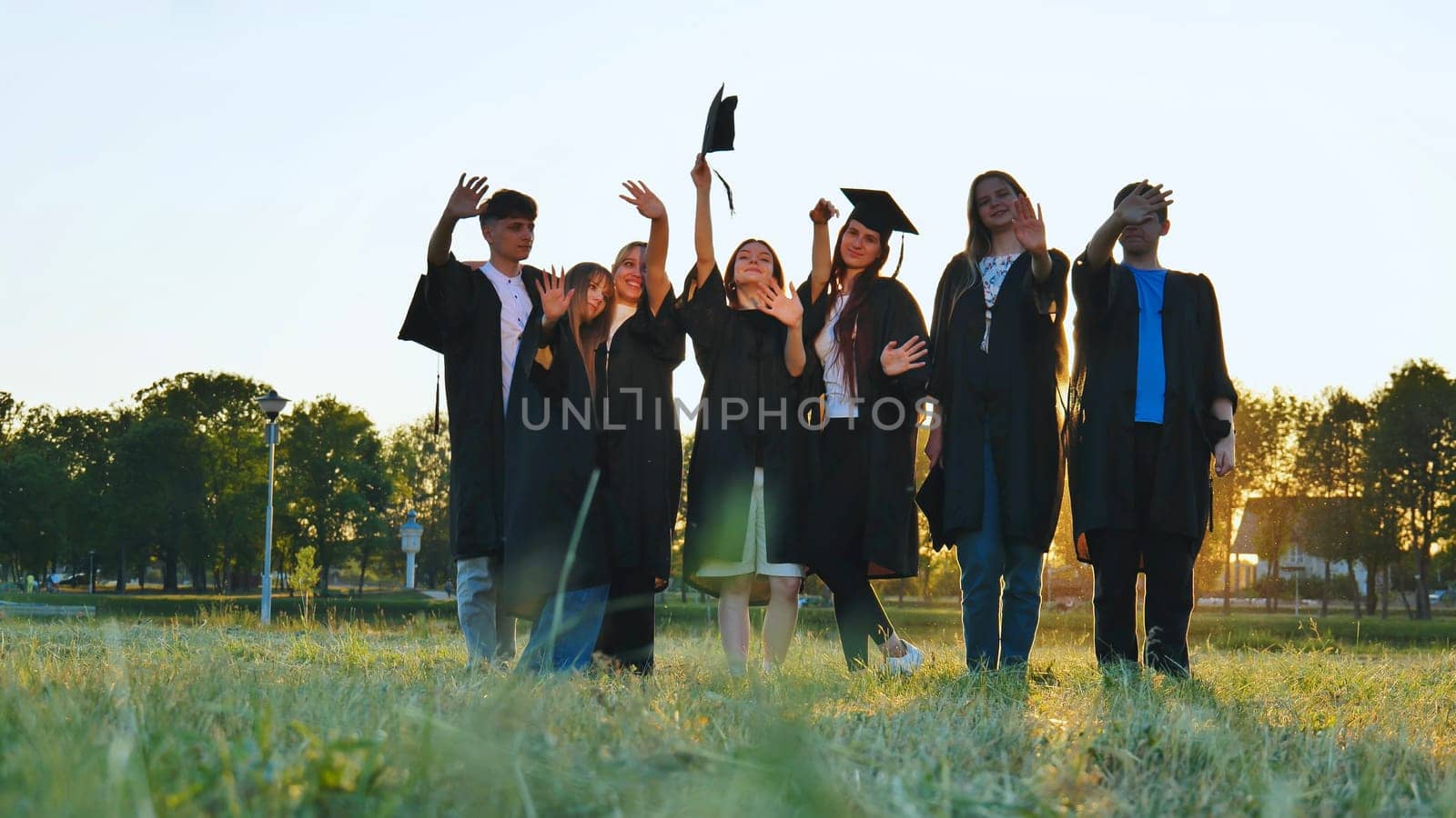 Student alumni waving at sunset. by DovidPro