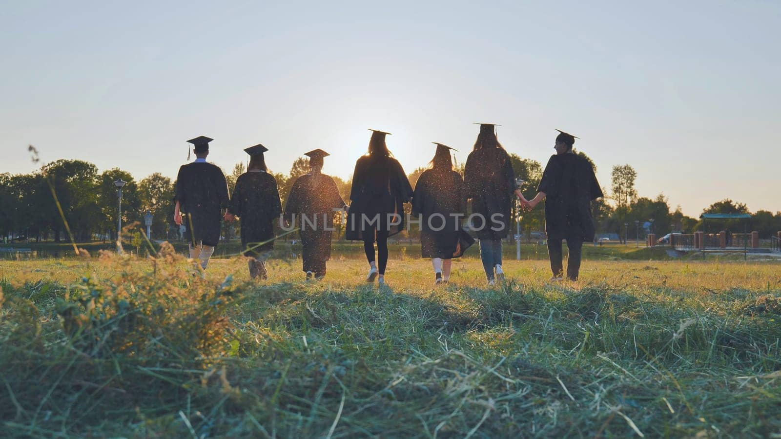 College graduates hold hands at sunset to meet the future and the sun