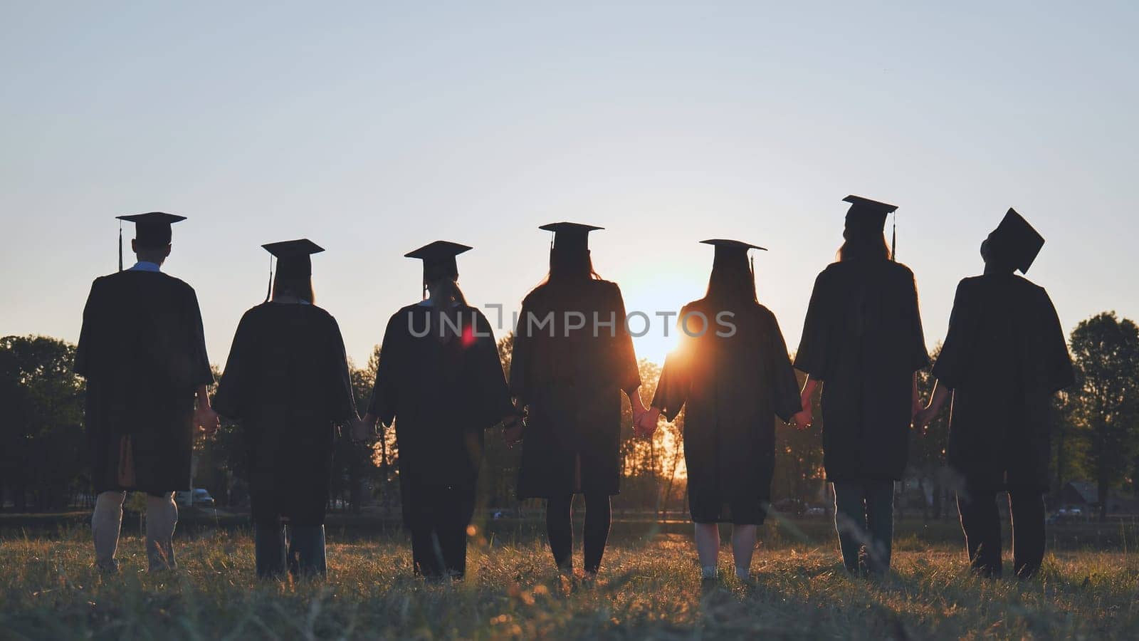 Silhouettes of college graduates standing in a meadow