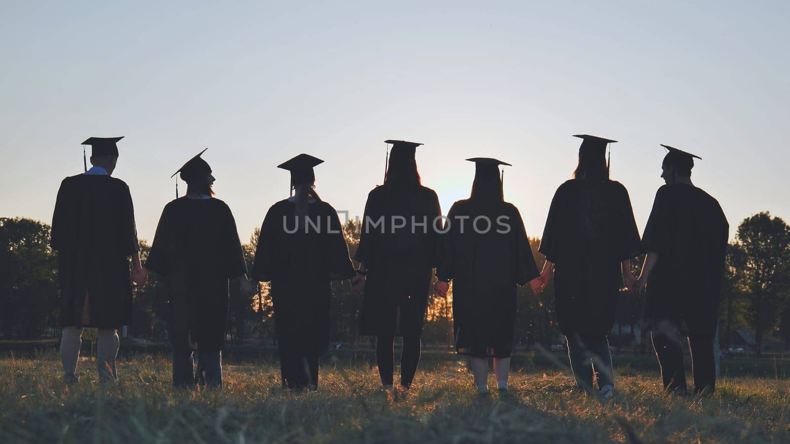 Silhouettes of college graduates standing in a meadow