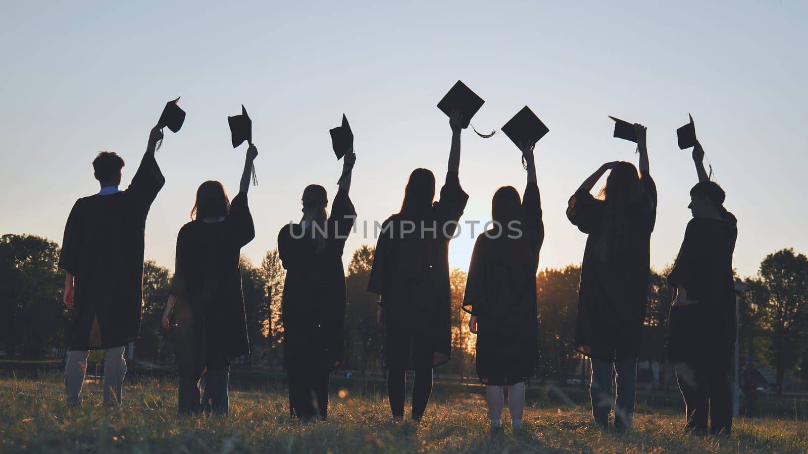 Silhouettes of college graduates waving their caps at sunset