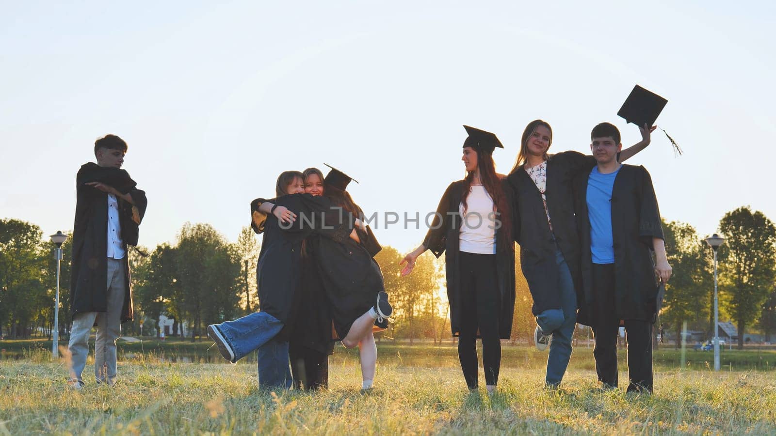 Student alumni waving at sunset. by DovidPro