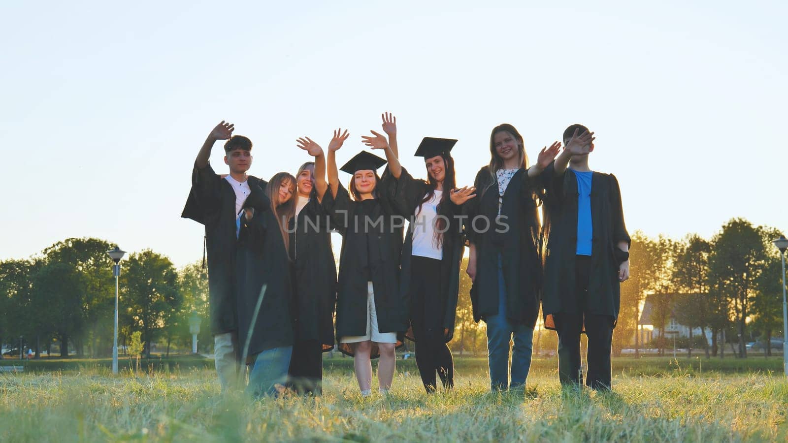 Student alumni waving at sunset. by DovidPro