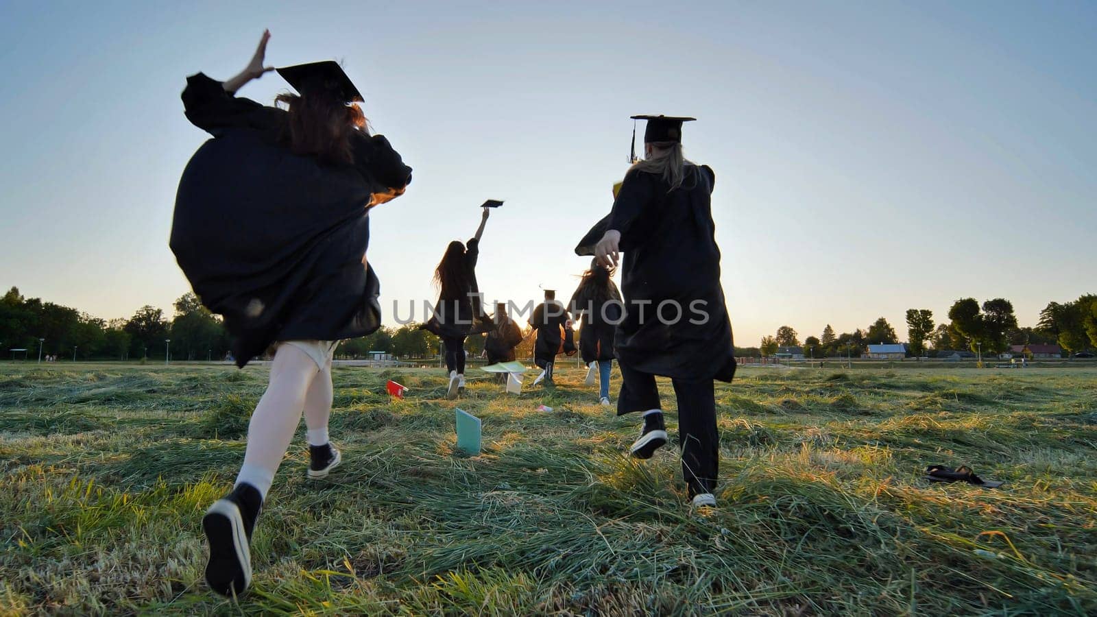 Cheerful graduates students run after school at sunset