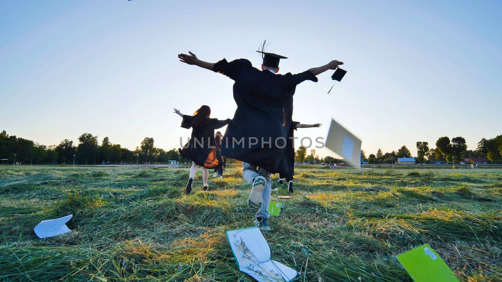 Cheerful graduates students run throwing notebooks after school at sunset. by DovidPro