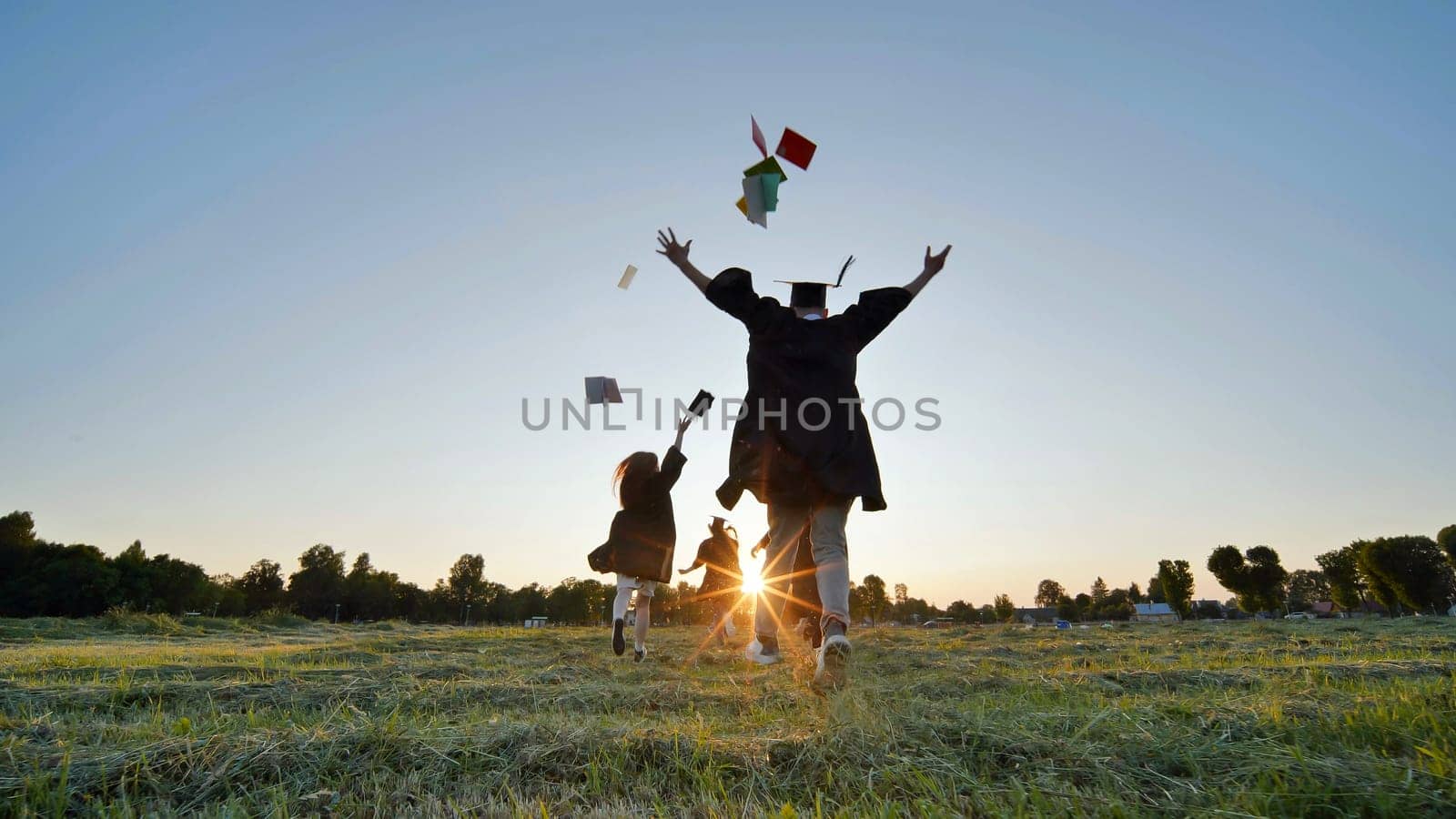 Cheerful graduates students run after school at sunset. by DovidPro