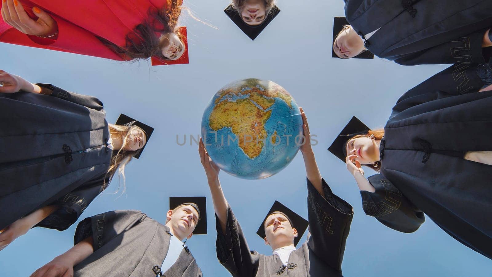 College graduates stand in a circle and hold a geographical globe of the world. by DovidPro