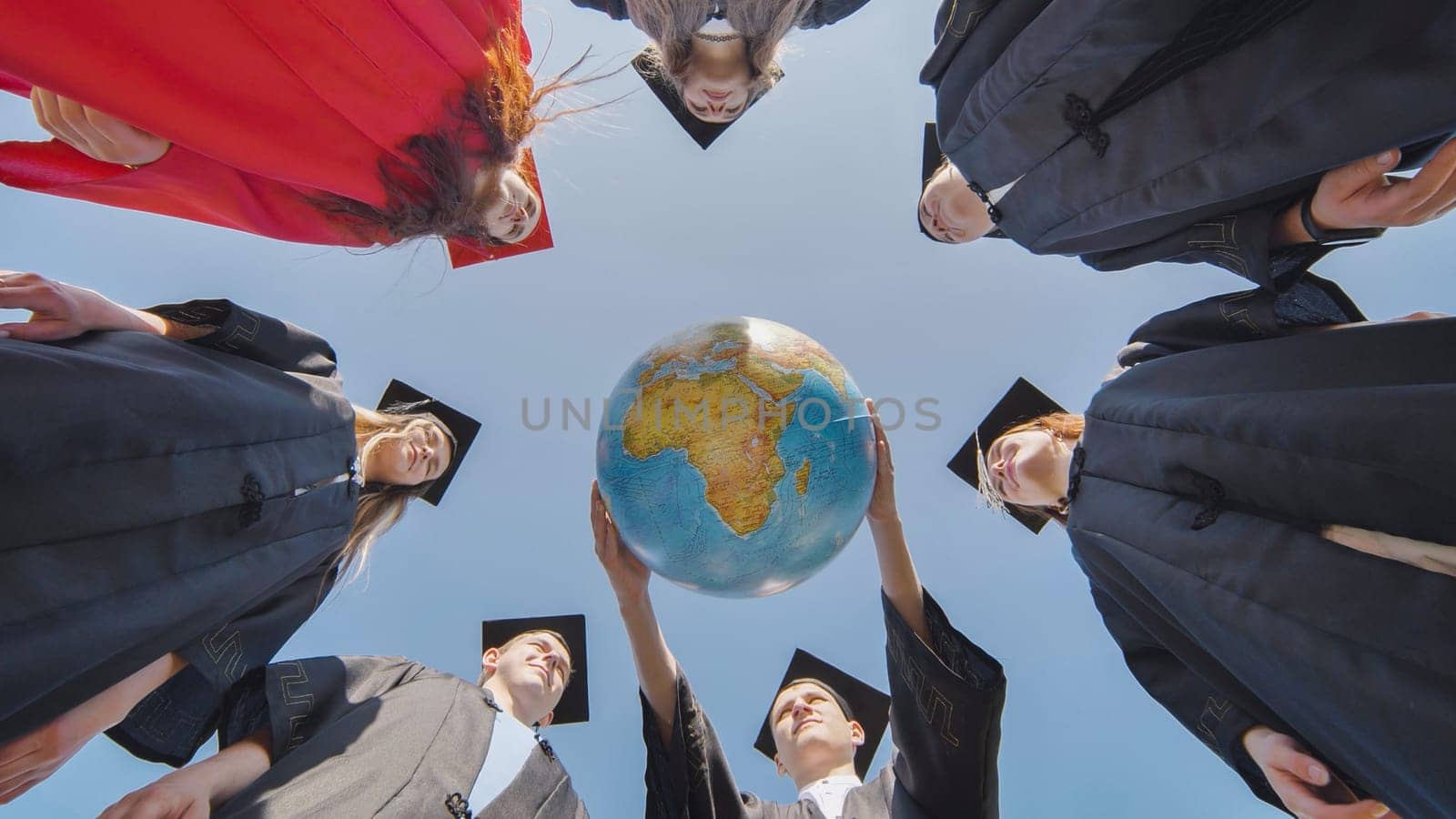 College graduates stand in a circle and hold a geographical globe of the world. by DovidPro