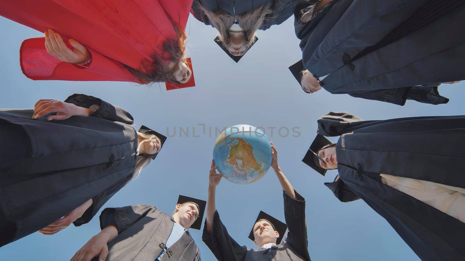 College graduates stand in a circle and hold a geographical globe of the world. by DovidPro