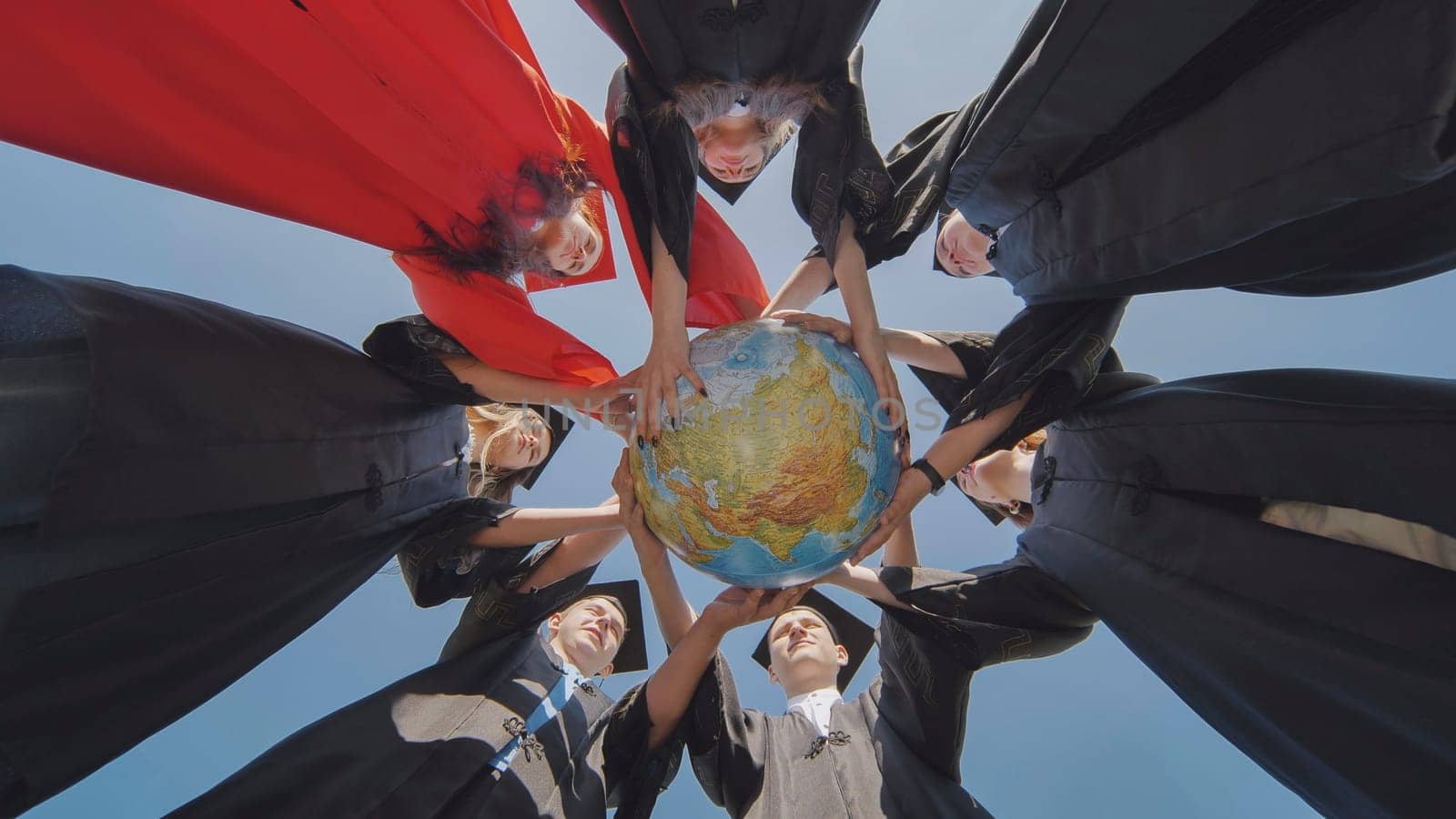 College graduates stand in a circle and hold a geographical globe of the world. by DovidPro