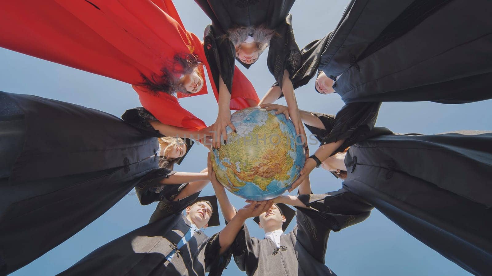 College graduates stand in a circle and hold a geographical globe of the world. by DovidPro