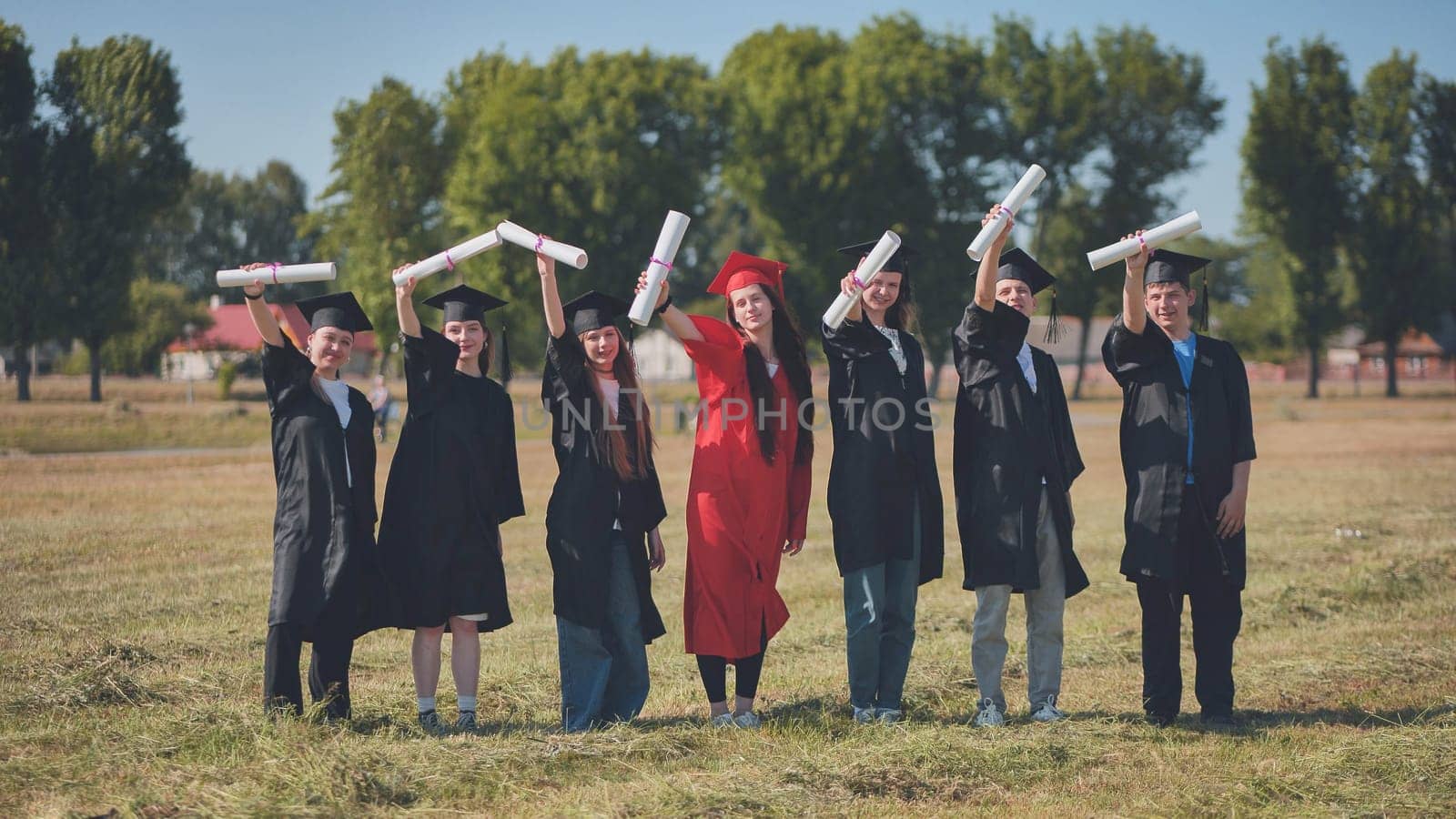 Young graduates pose with diplomas in hand on the street. by DovidPro