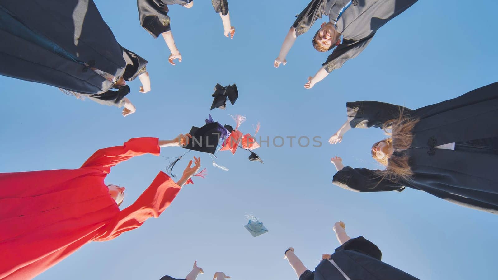 Graduates tossing multicolored hats against a blue sky