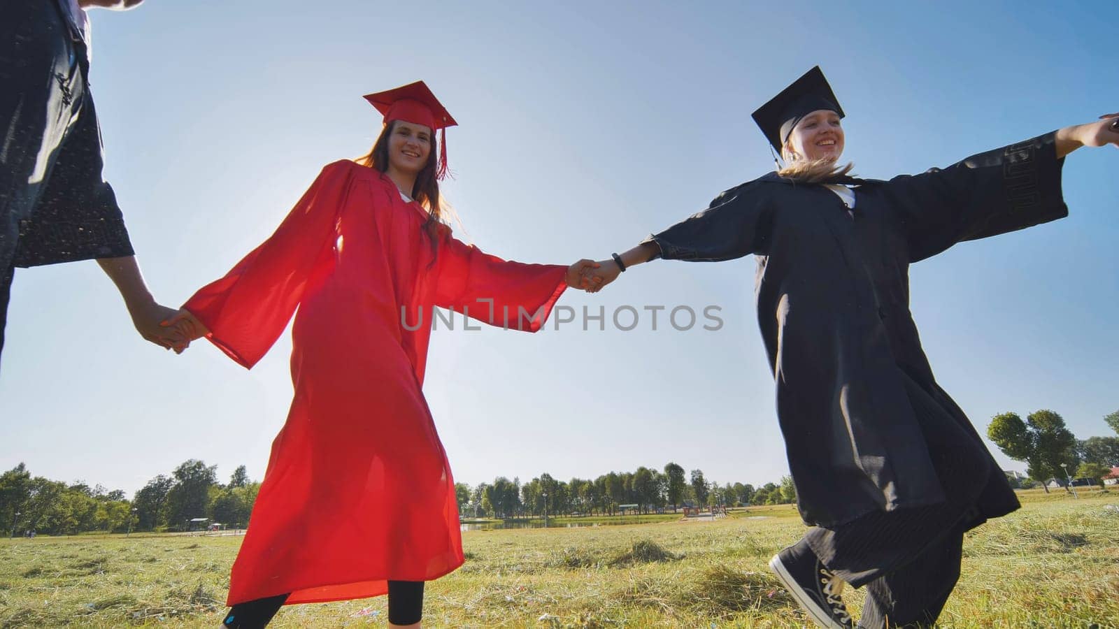 College graduates holding hands run in a round dance. by DovidPro