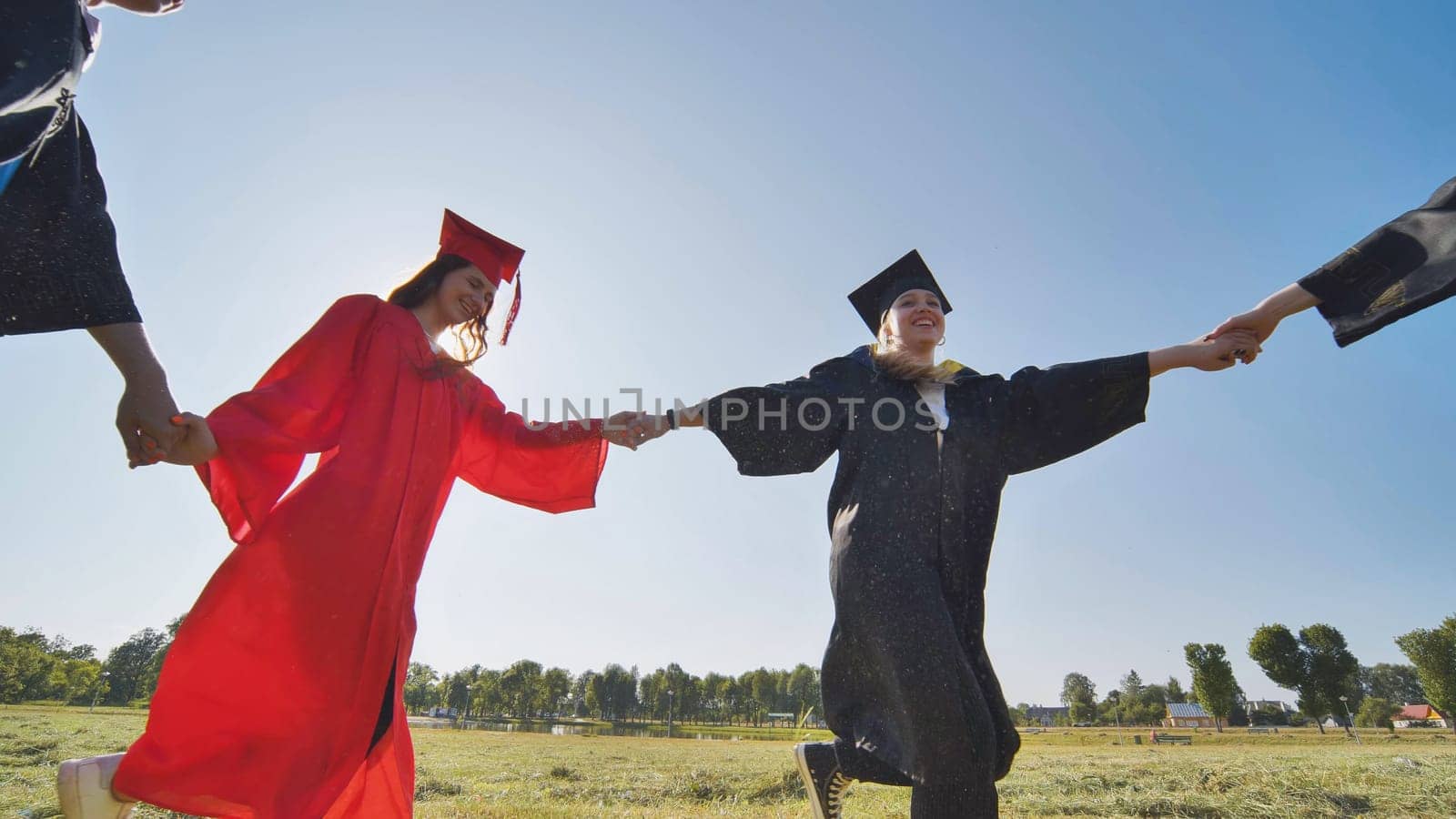 College graduates holding hands run in a round dance. by DovidPro