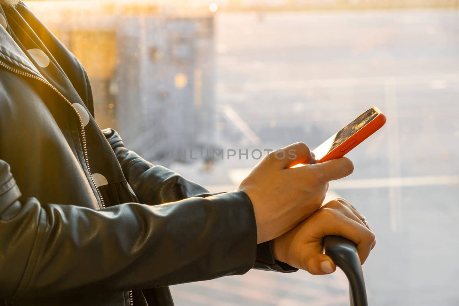 Woman in a black jacket checking her smartphone standing with a suitcase at the airport by vladimka