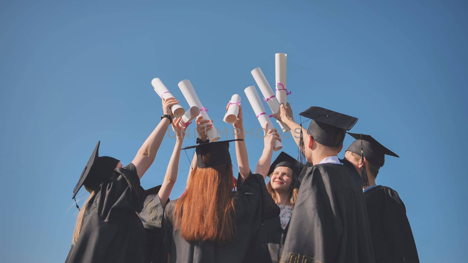 College graduates with caps tie their diplomas together. by DovidPro