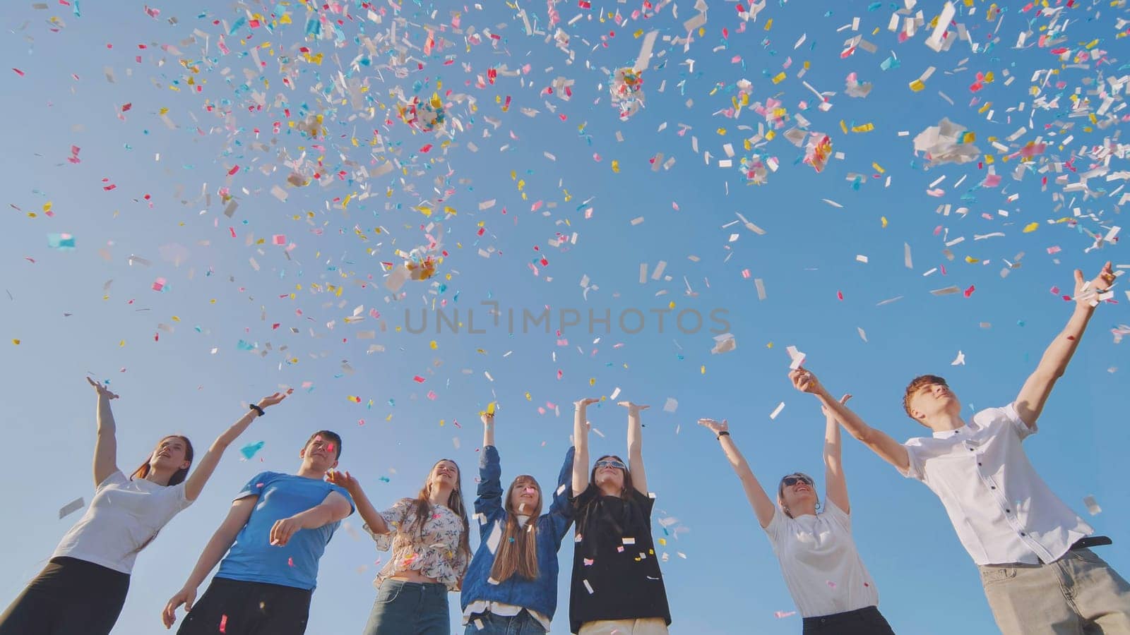 Friends toss colorful paper confetti from their hands. by DovidPro