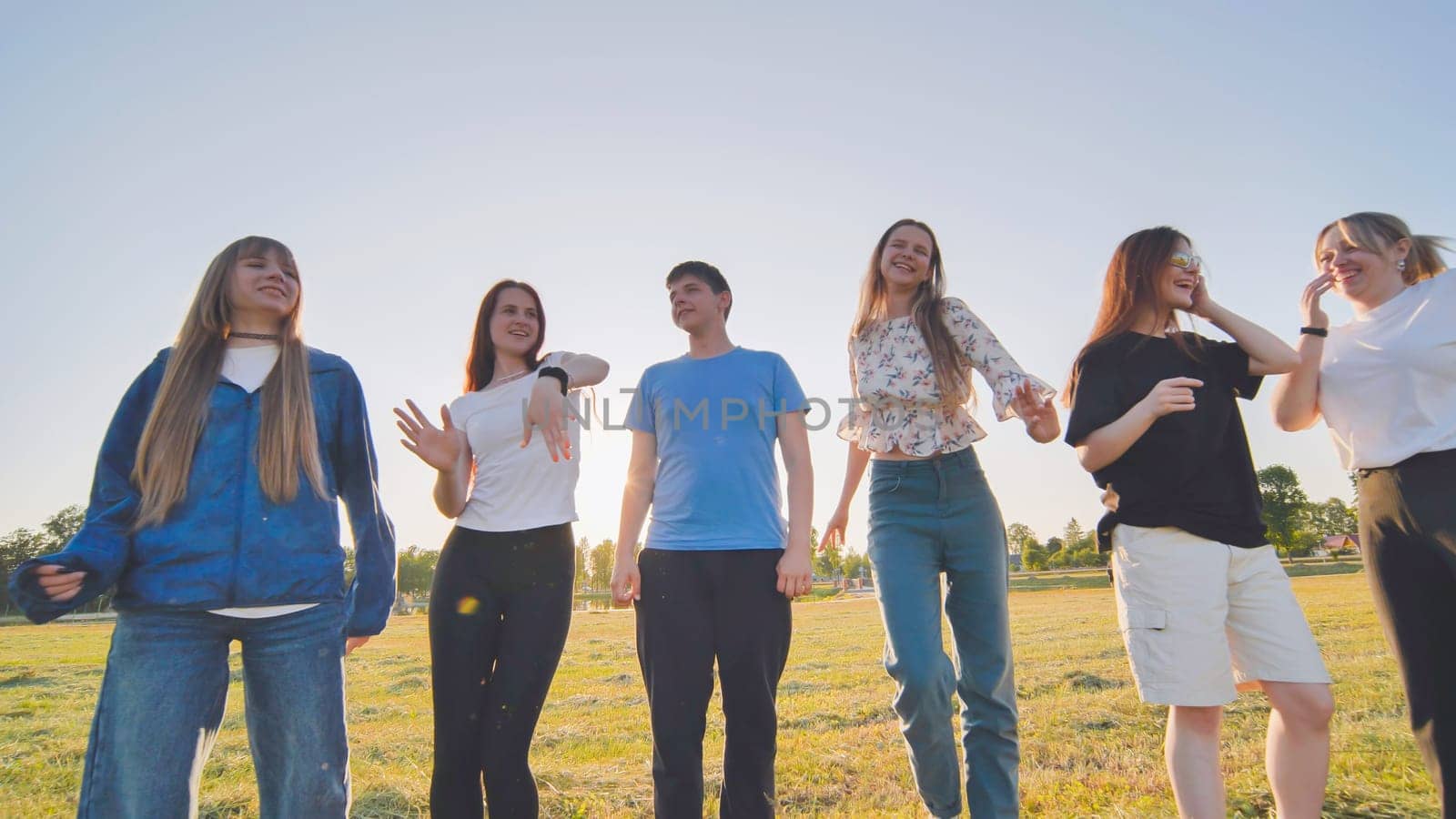 Funny jolly friends dancing in the city meadow in the evening