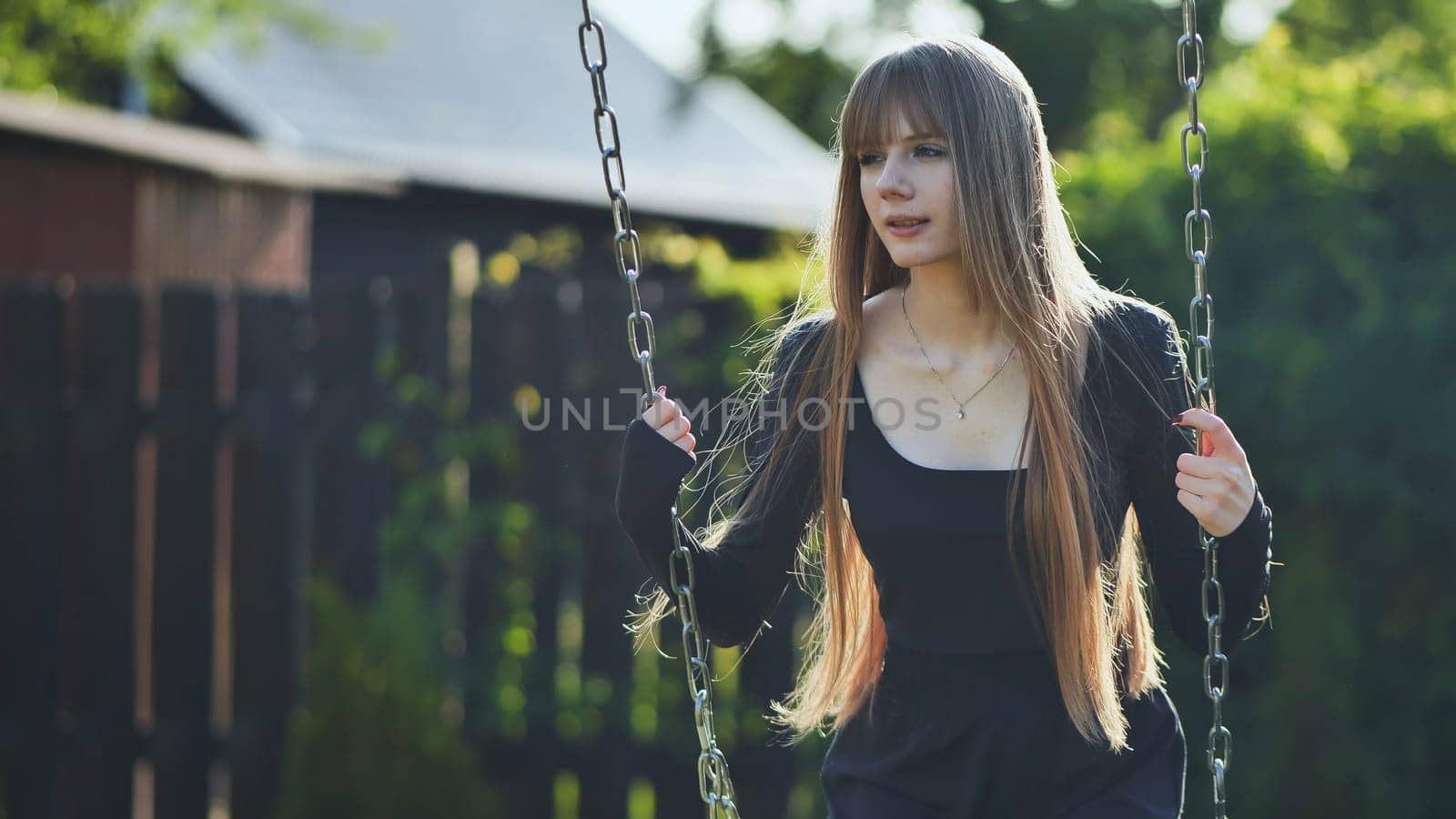 A blonde-haired girl in a black dress rides on a swing. by DovidPro