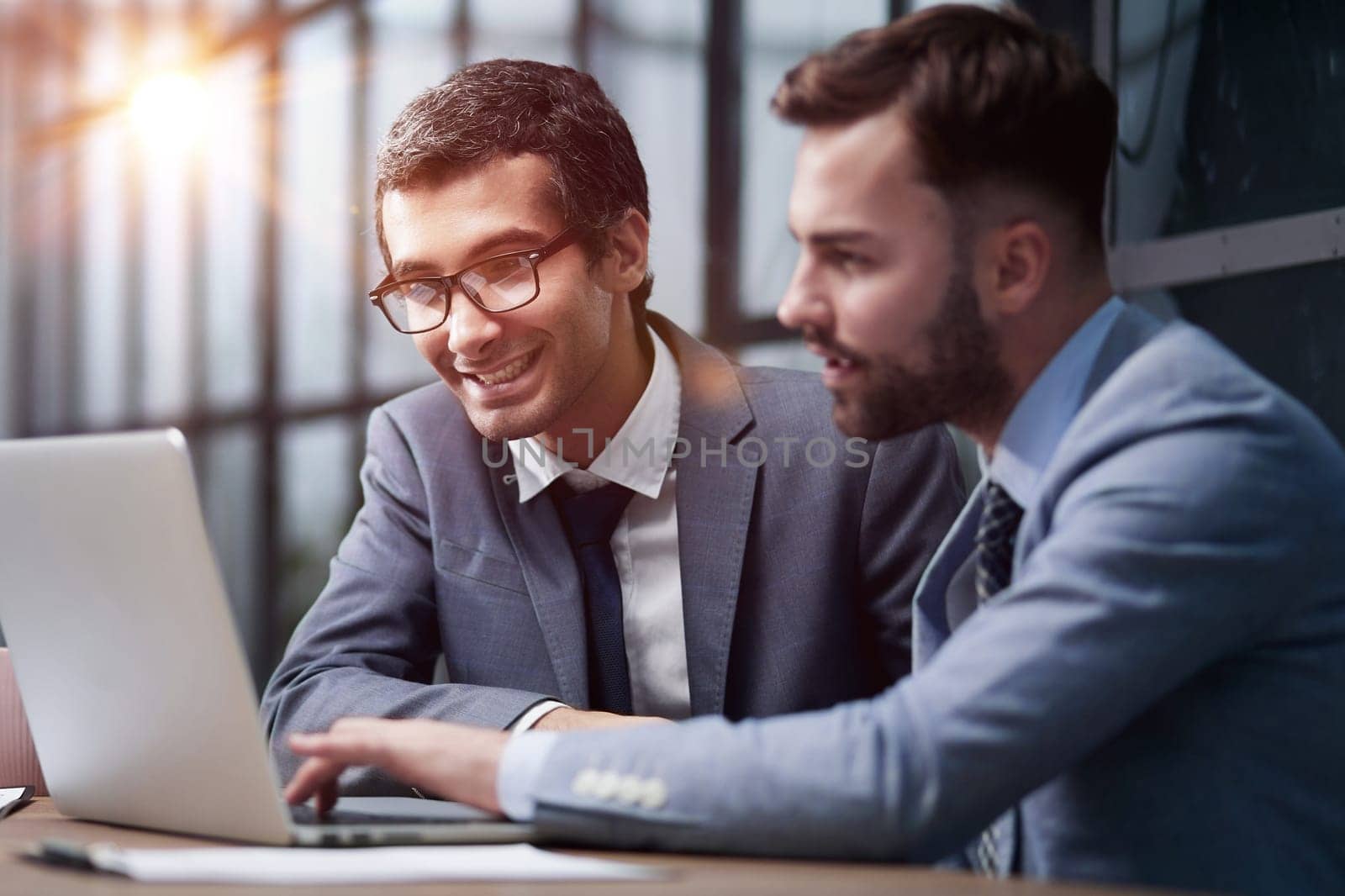 Two young businessmen sitting at workplace and working together in office by Prosto