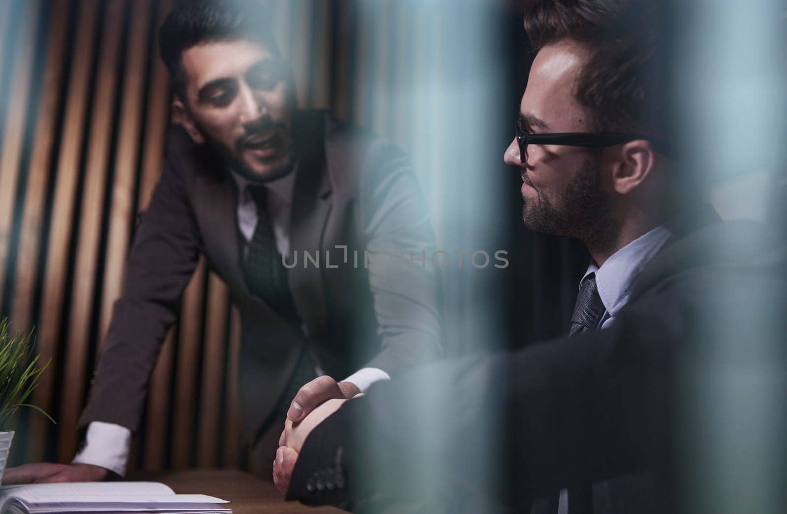 Two positive confident businessmen shaking hands over meeting table after negotiation, by Prosto