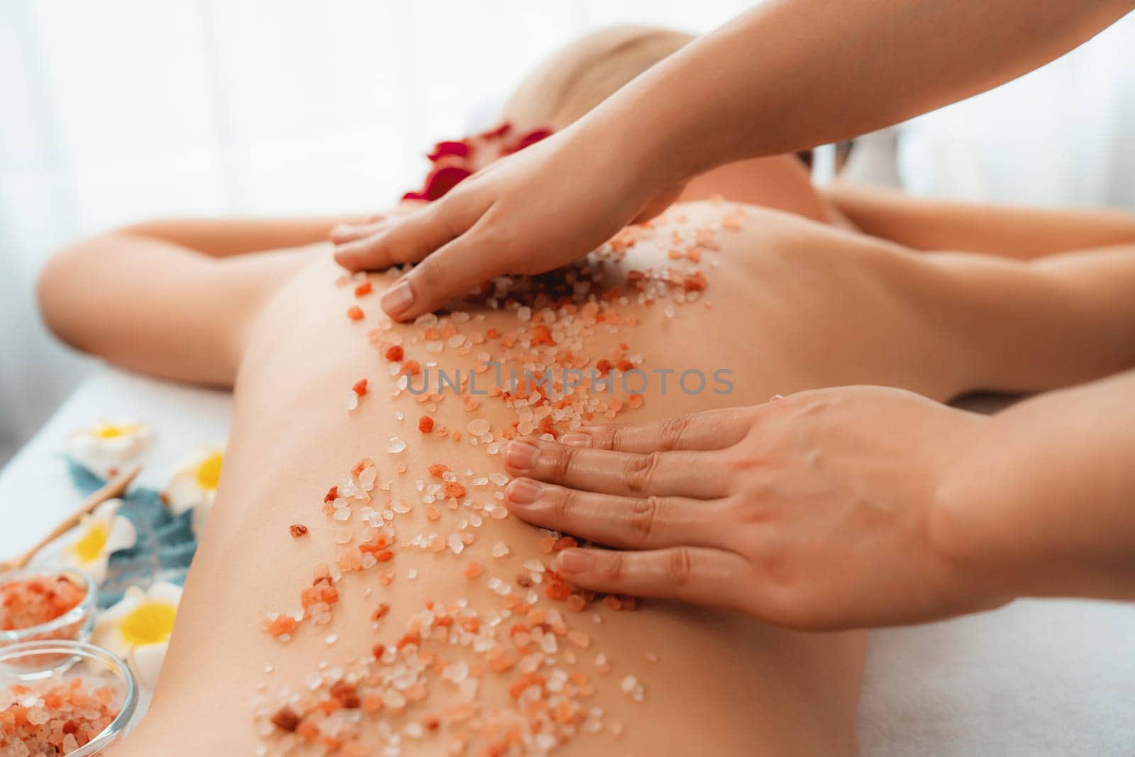 Closeup woman customer having exfoliation treatment in luxury spa salon with warmth candle light ambient. Salt scrub beauty treatment in health spa body scrub. Quiescent