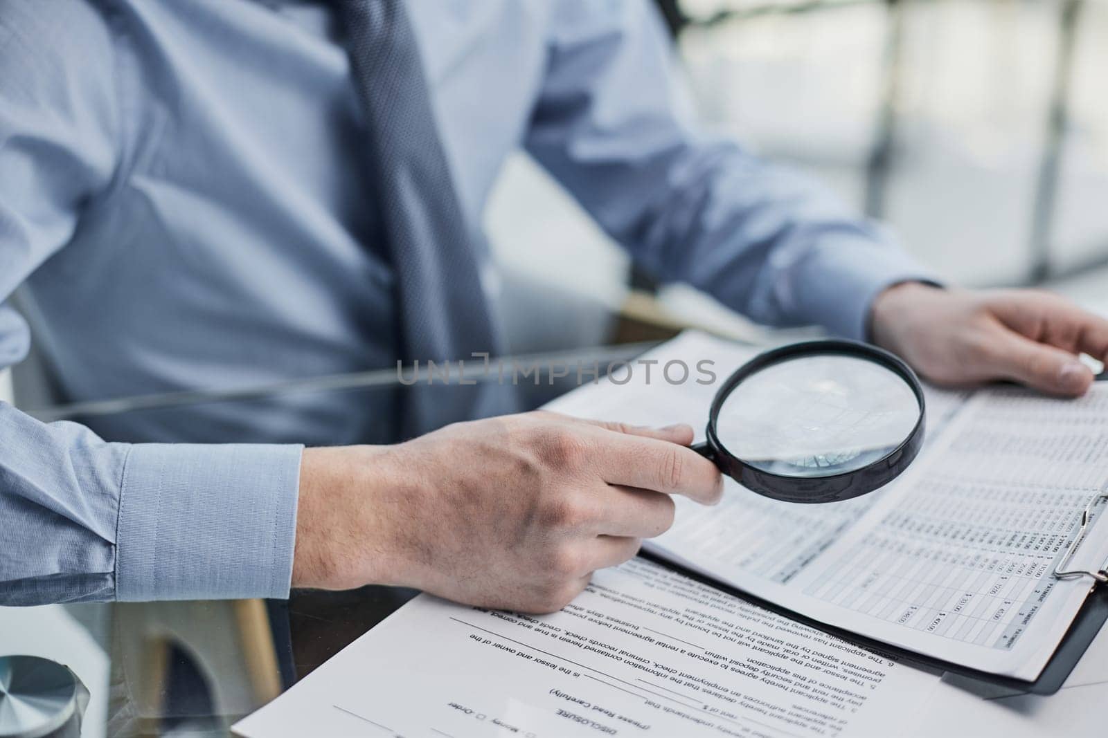 Businessman looking through a magnifying glass to documents by Prosto