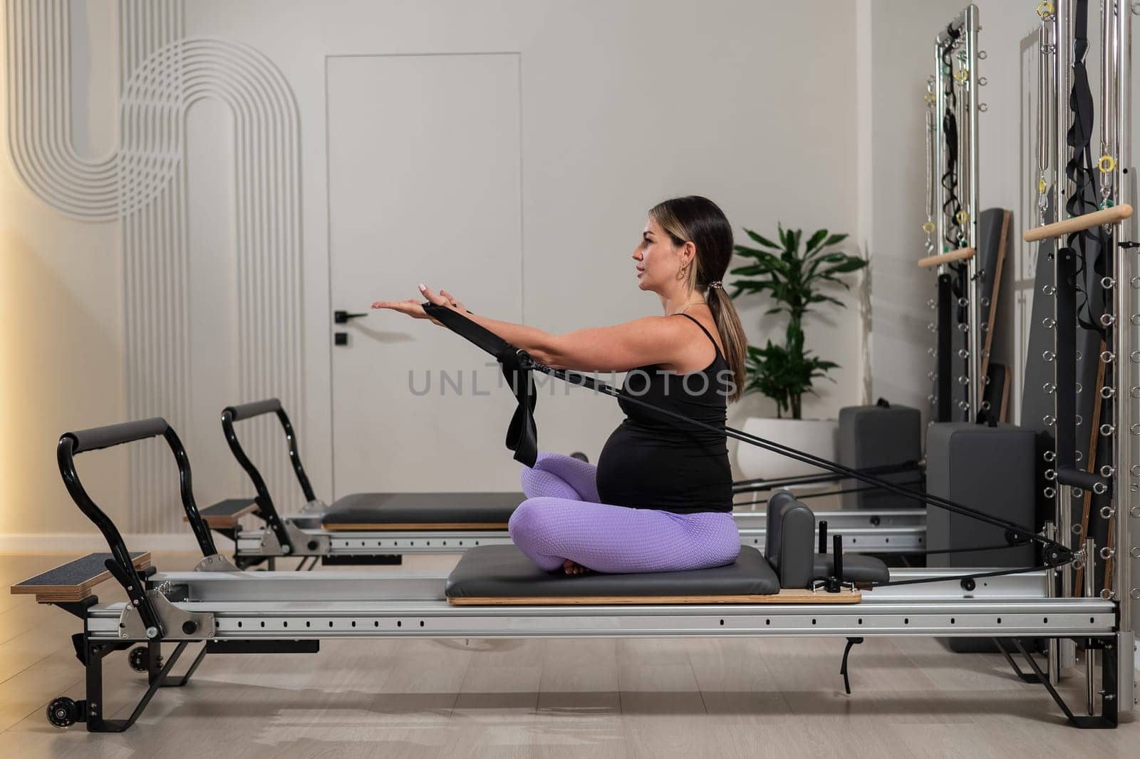 Pregnant woman doing Pilates exercises on a reformer machine. by mrwed54
