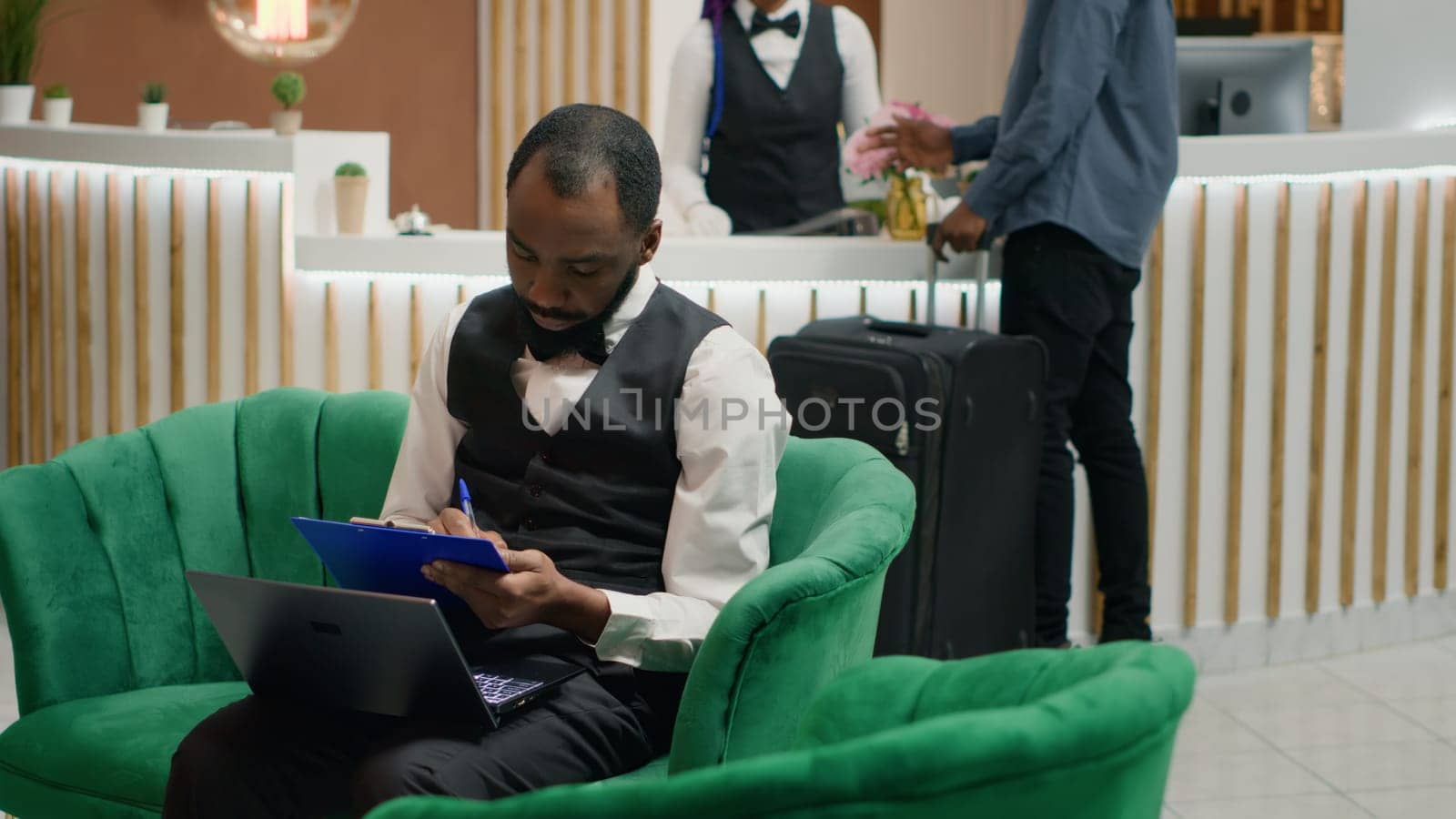 Tourism industry employee. Bellboy entering data document forms on papers in lounge area, hotel concierge making entry in daily luggage movement register, using clipboard notes.