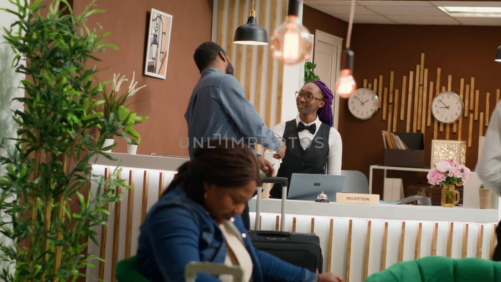 Hotel guest getting access room card after check in process at reception, meeting with front desk staff asking about ammenities. African american man travelling on holiday at resort. Handheld shot.