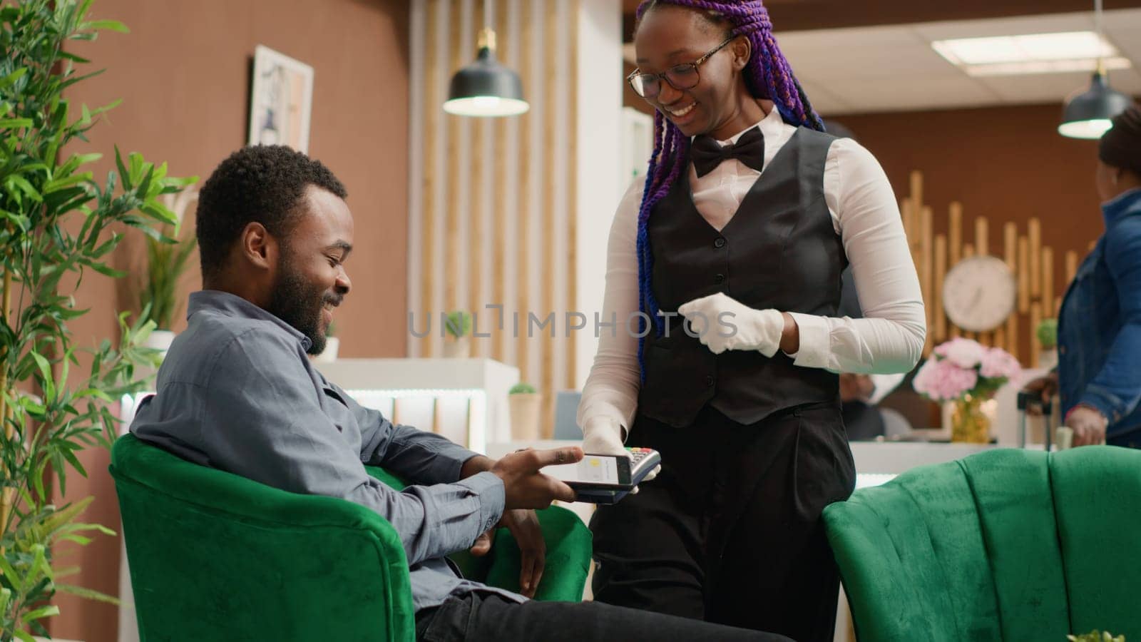 Man does mobile payment at pos, using nfc system to pay for cup of coffee in lounge area at five star hotel. Guest shows gratitude to staff member after providing excellent service. Handheld shot.