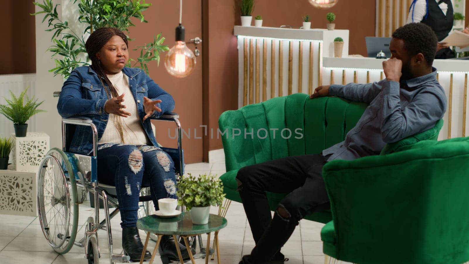 African american wheelchair user sitting in lounge area and waiting for room check in with husband, dealing with chronic disability and travelling on honeymoon together. Physical impairment.