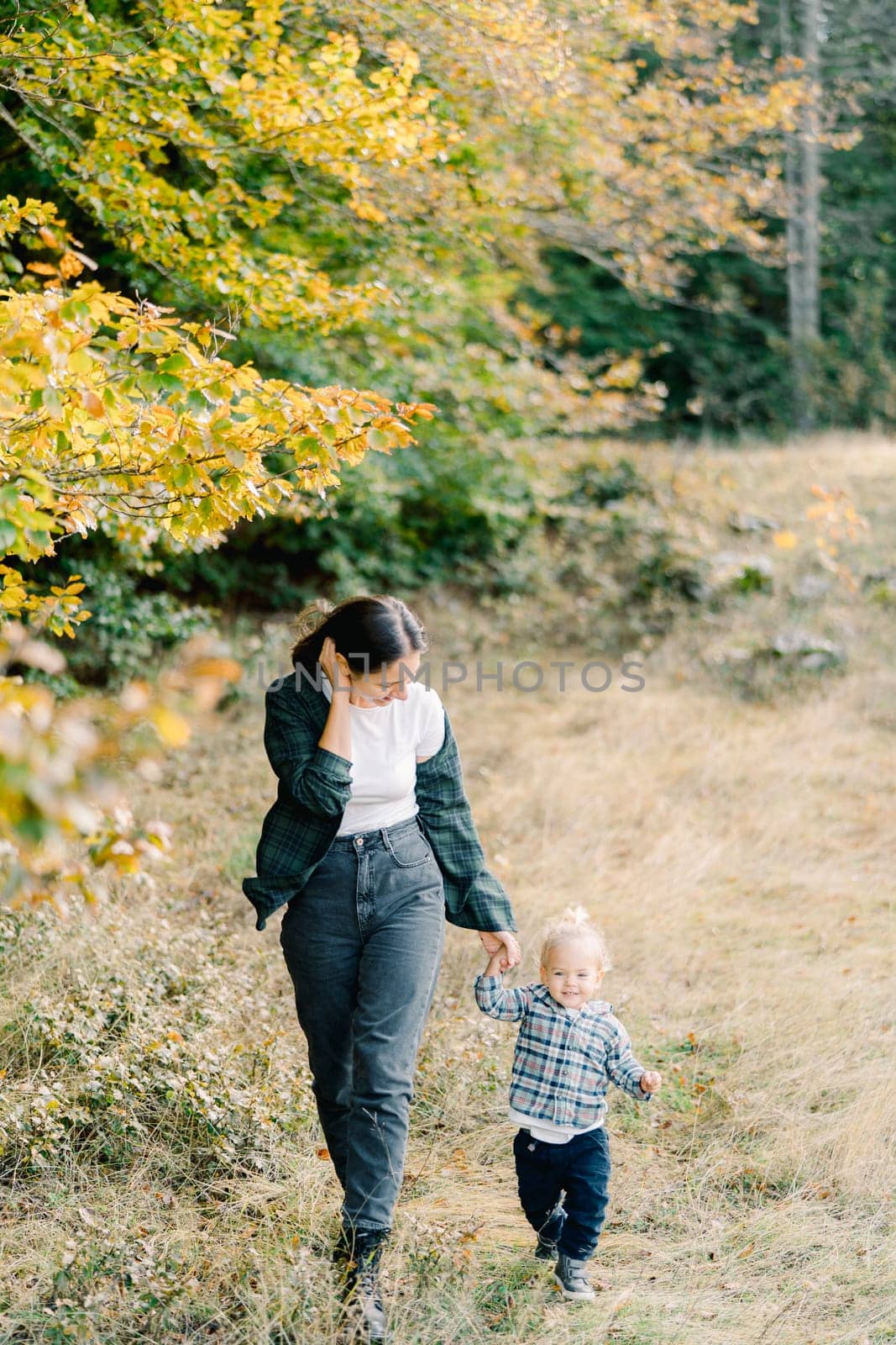 Mom leads a little girl by the hand, straightening her hair, walking through the autumn forest. High quality photo