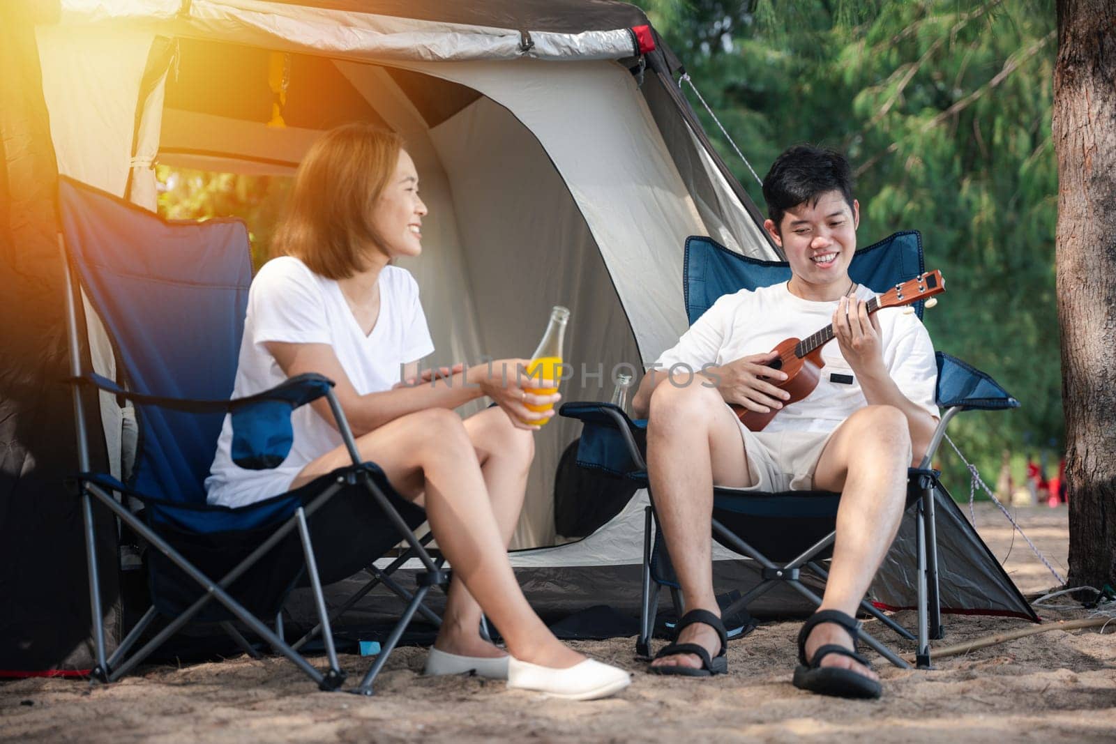 An outdoor serenade, A beaming Asian couple, by their tent, shares a song on the ukulele, capturing the essence of togetherness and happiness. Music and love unite at the campsite. Camping putdoor by Sorapop