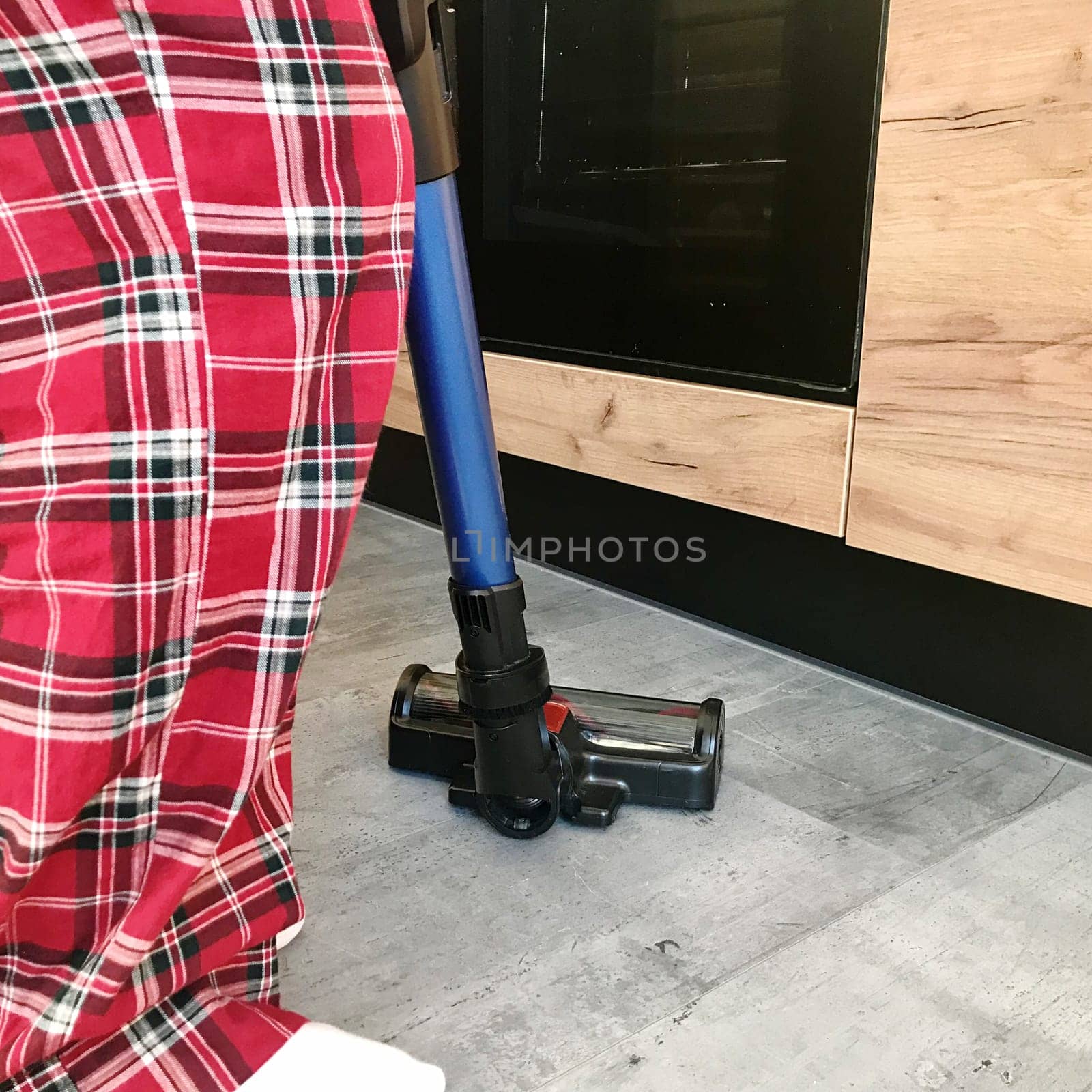 A woman in checkered pajamas is cleaning the gray floor with a vacuum cleaner. High quality photo