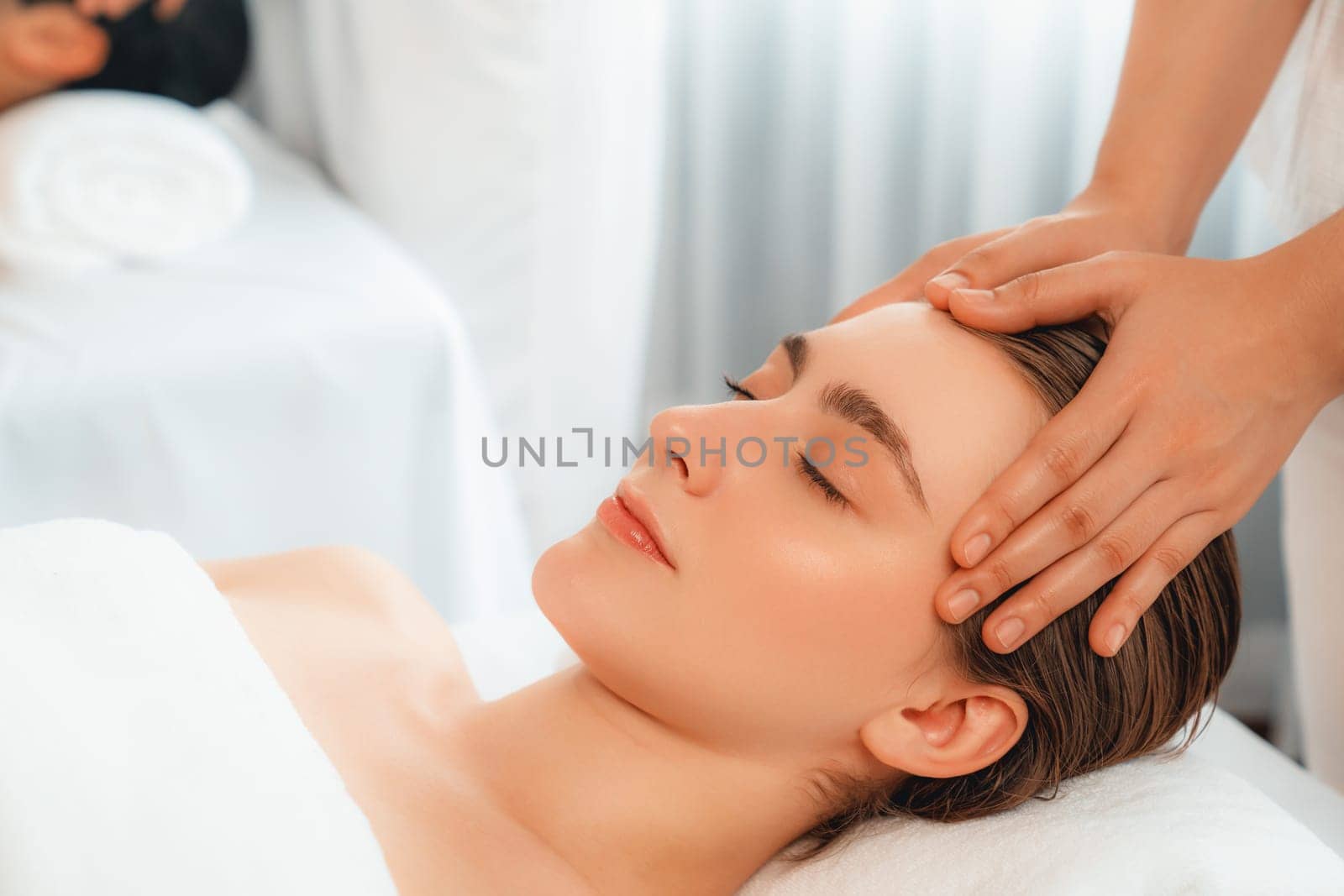 Caucasian couple enjoying relaxing anti-stress head massage and pampering facial beauty skin recreation leisure in dayspa modern light ambient at luxury resort or hotel spa salon. Quiescent