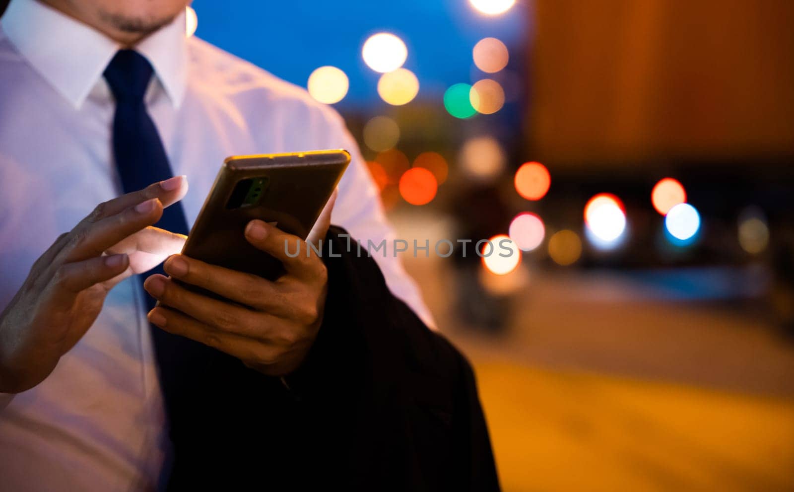 Young man walking and chatting on mobile phone with friends at social networks outdoor, Portrait Asian businessman typing an sms message via smartphone after work near office at night city street