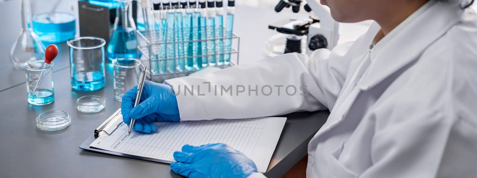 Closeup hand recording clinical data result after conducting chemical experiment in medical laboratory for vaccine drug or antibiotic. Scientific chemistry lab and medicine research concept. Neoteric