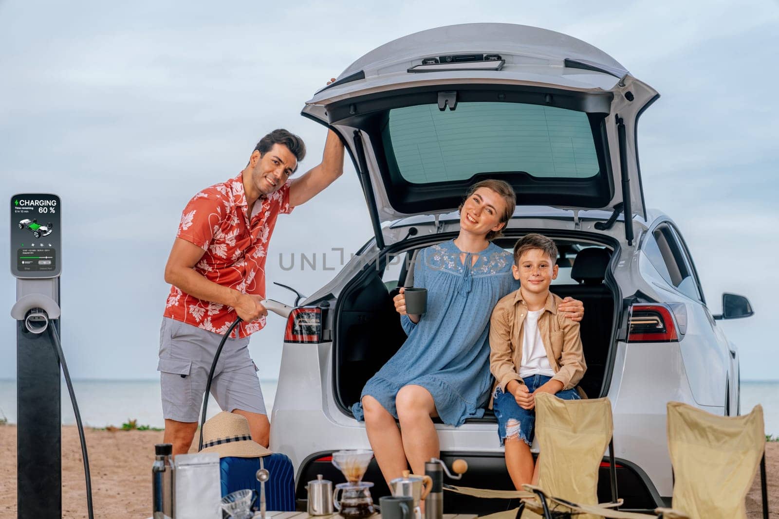 Family vacation trip traveling by the beach with electric car, happy family recharge EV car, enjoying outdoor camping coffee. Seascape travel and eco-friendly car for clean environment. Perpetual